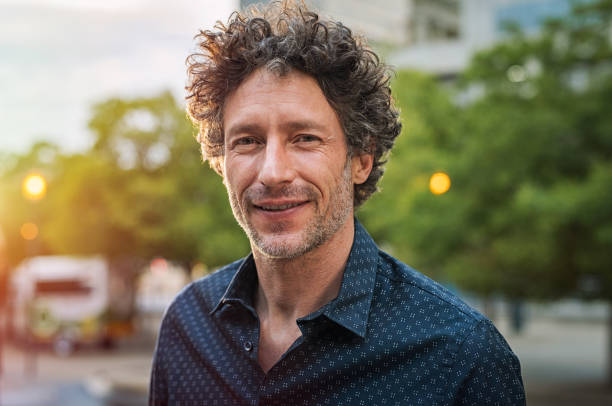 Portrait of happy mature man looking at camera outdoor. Senior businessman with beard feeling confident at sunset. Closeup face of business man smiling with city in background.