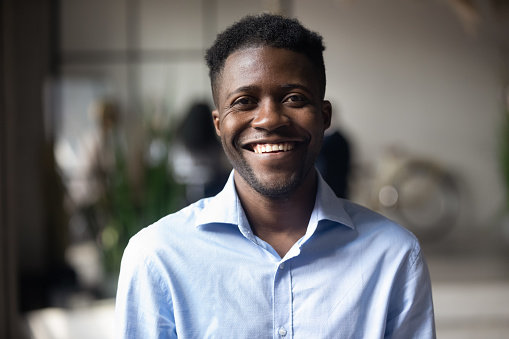 Confident smiling millennial african american businessman looking at camera in modern office, happy male professional company leader coach trainer posing alone, close up head shot business portrait